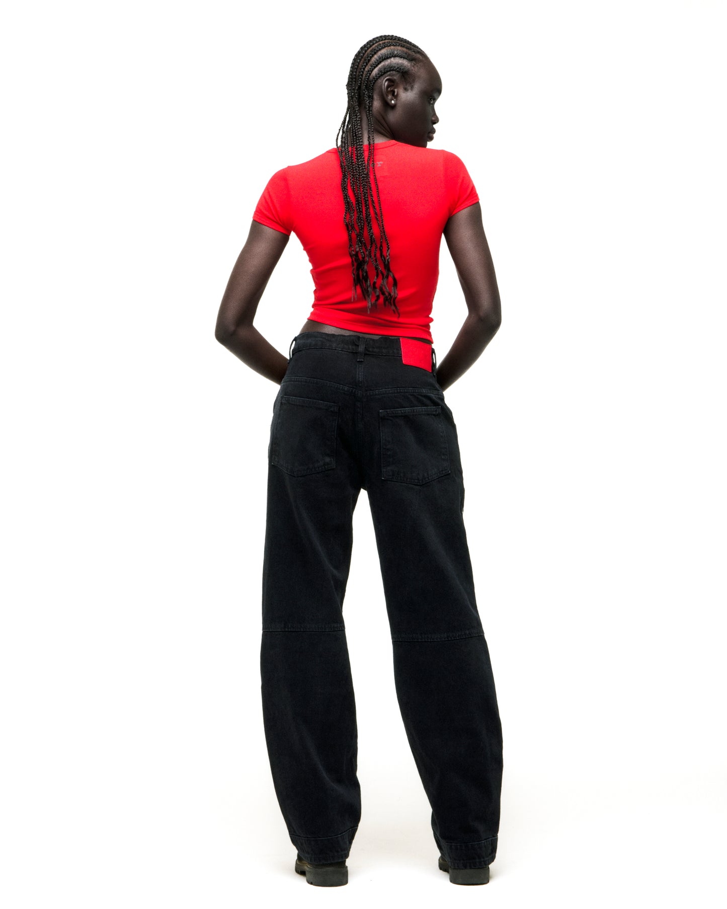 Model from behind wearing a cropped red cotton/spandex baby tee and baggy black jeans.