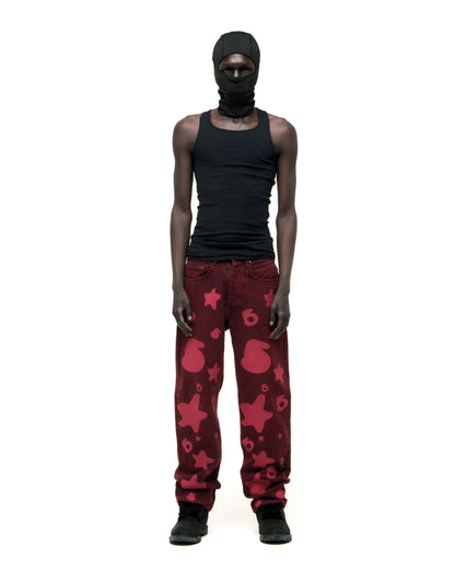 Model wearing faded wash Beluga print red denim pants with custom hardware and a branded leather patch.