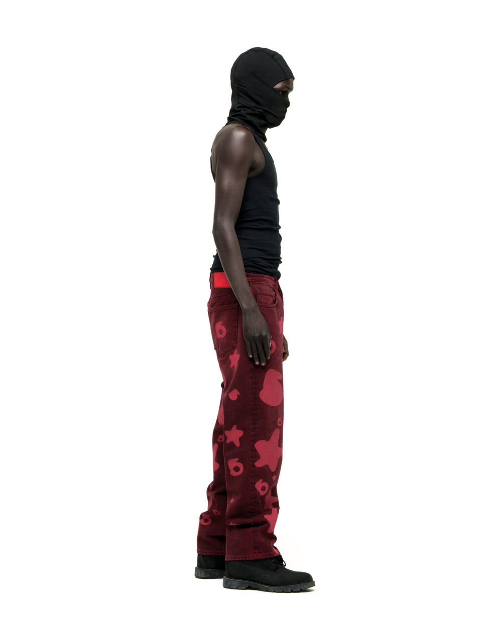 Man in black balaclava and tank top wearing faded red denim pants with Beluga print, custom hardware, and straight leg fit.
