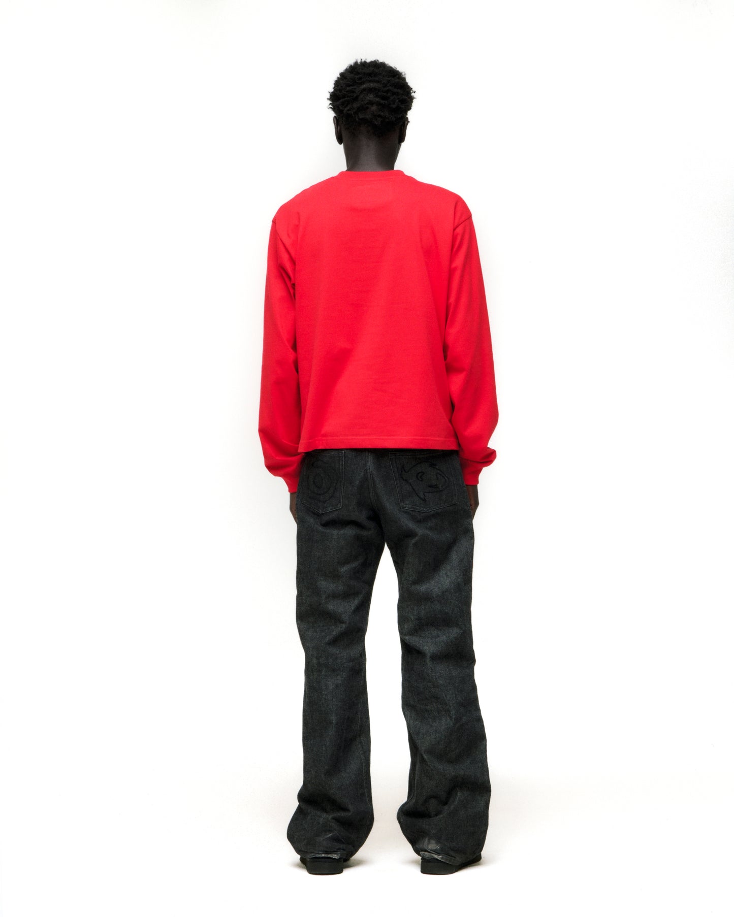 Back view of a model wearing a red 555 SP5DER cotton long sleeve tee with ribbed cuffs.