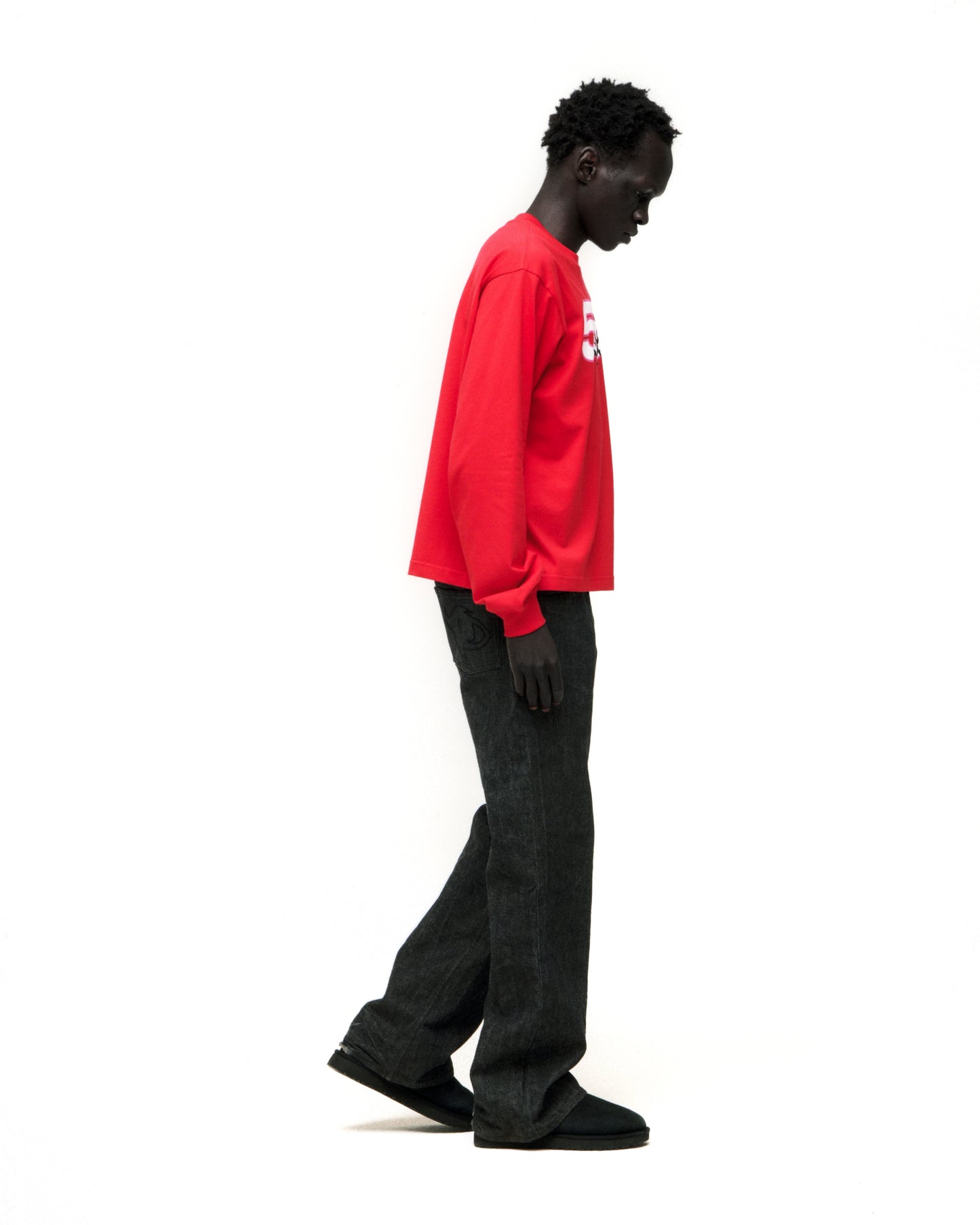Man in red 555 SP5DER LONGSLEEVE with white graphic print, black jeans, and black shoes.