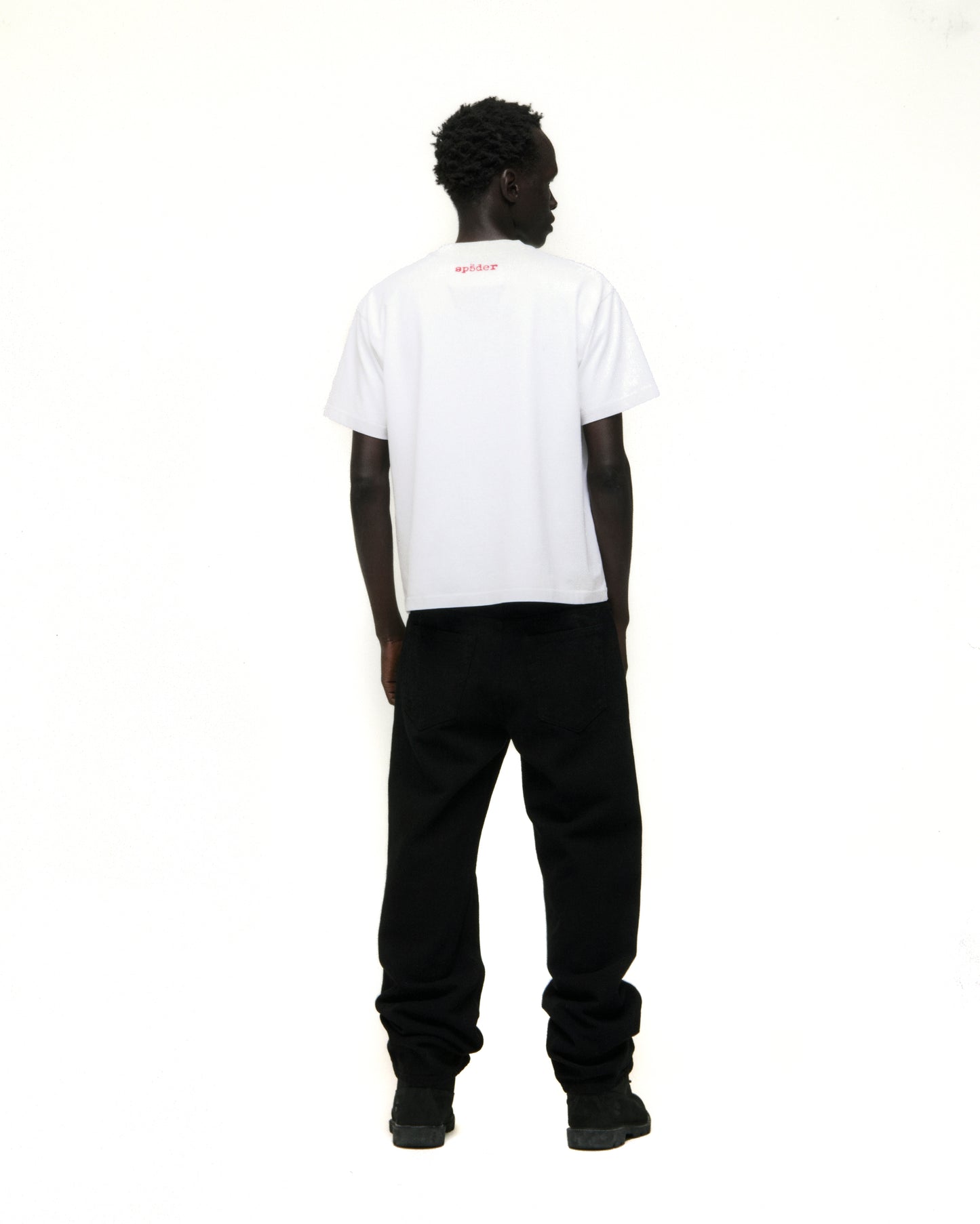 Model from behind wearing a white Vivienne Tee with red 'SP5DER' logo on back neck and black pants.