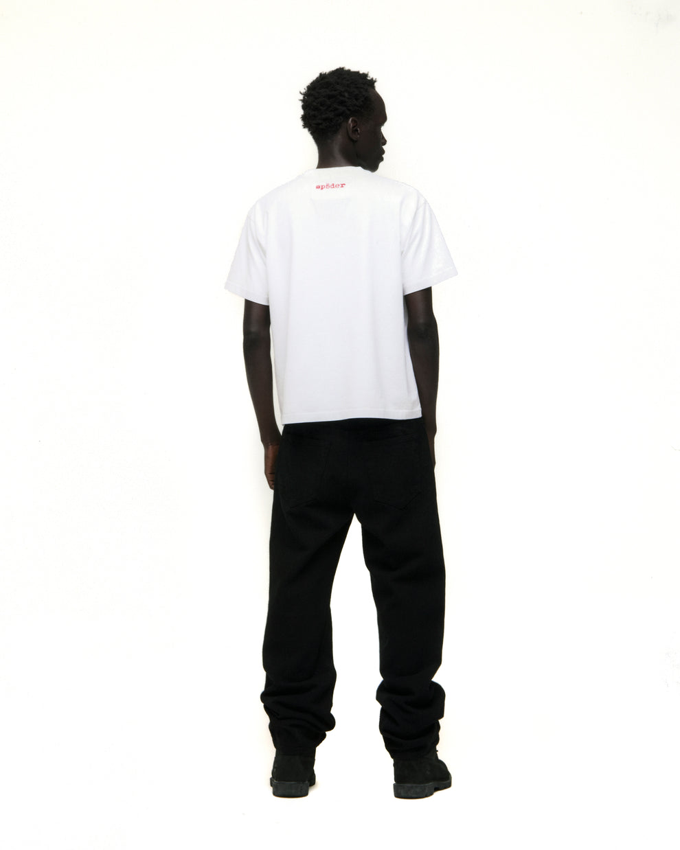 Model from behind wearing a white Vivienne Tee with red 'SP5DER' logo on back neck and black pants.