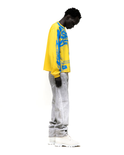 Yellow SP5 WINNERS LONGSLEEVE with blue graphic print, worn by a model in light grey jeans and white boots.