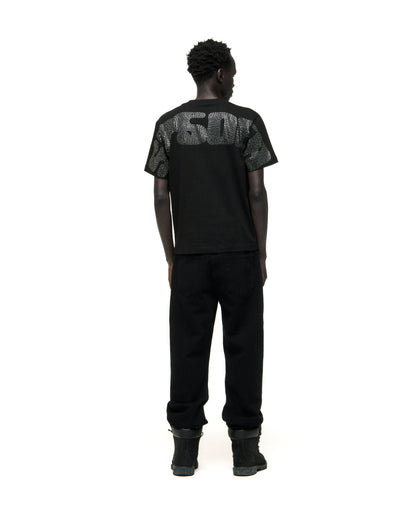 Man in black cotton rhinestone embellished tee with graphic on back, paired with black pants and boots.