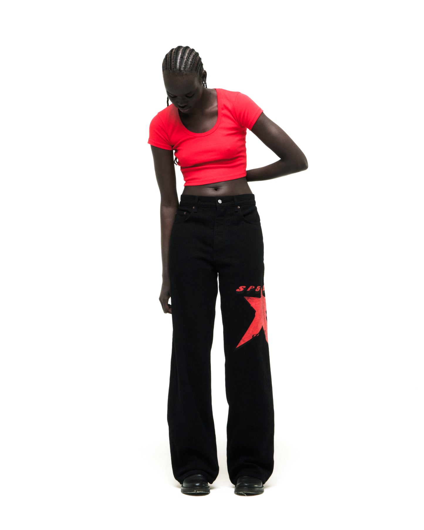 Black denim pants with a large red star graphic on the upper leg, worn by a model.