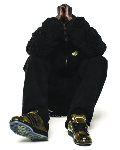 Person in black outfit, wearing SP5DER x ADIDAS SUPERSTAR sneakers with glossy gold cracked patent leather and translucent blue outsoles.