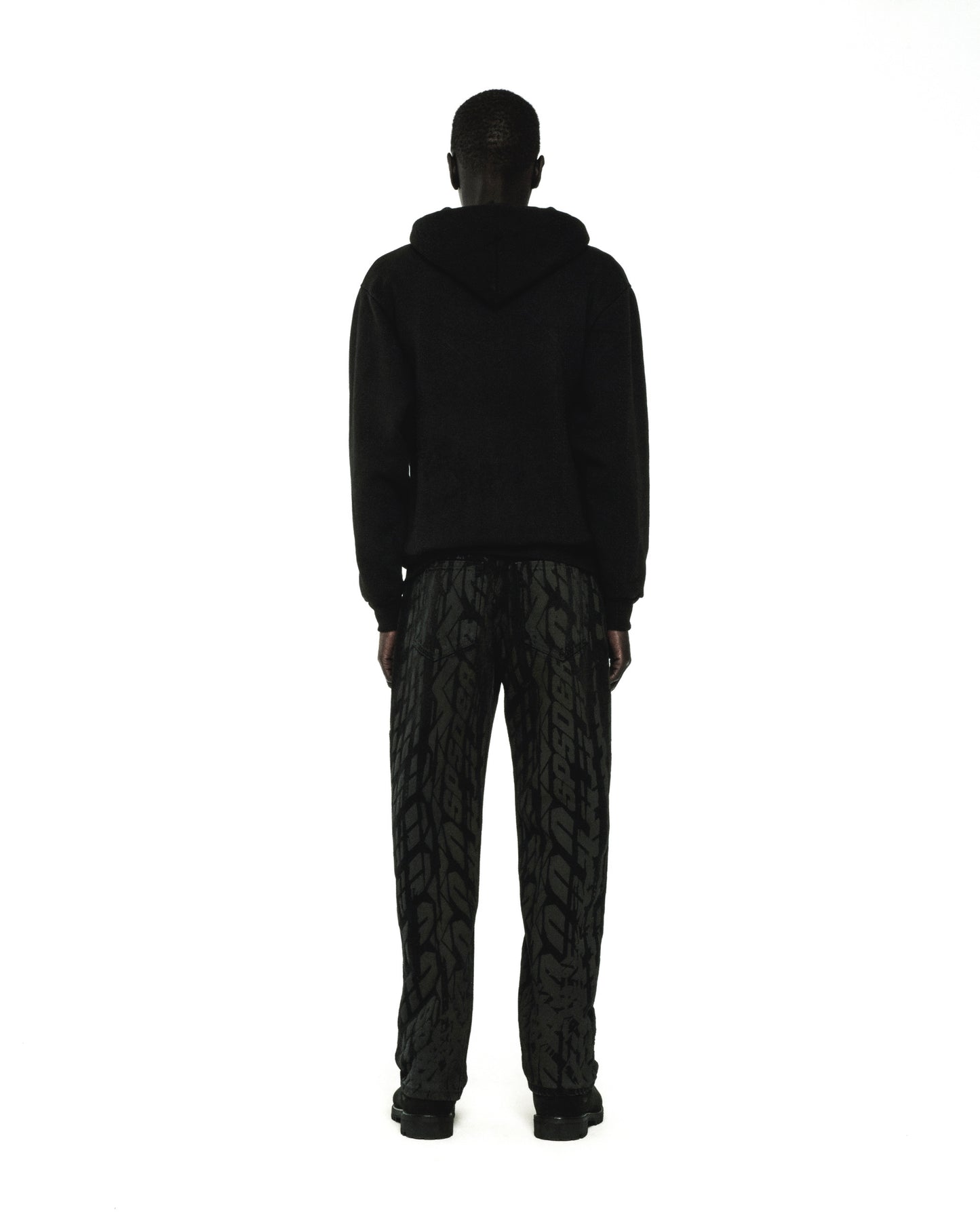 Man in black fleece hoodie and patterned pants, rear view.