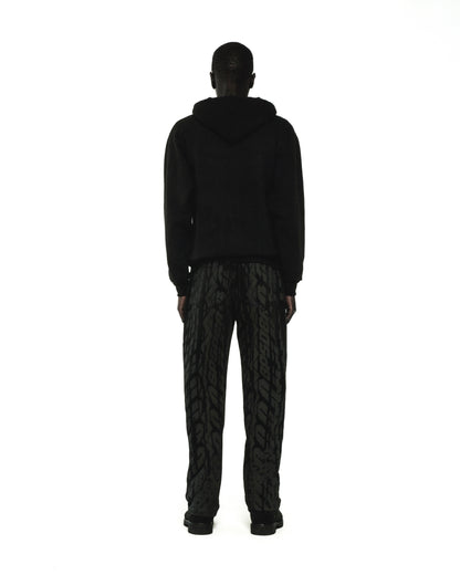 Man in black fleece hoodie and patterned pants, rear view.