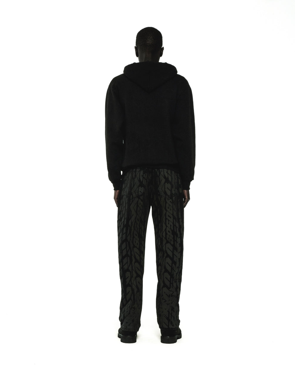 Man in black fleece hoodie and patterned pants, rear view.