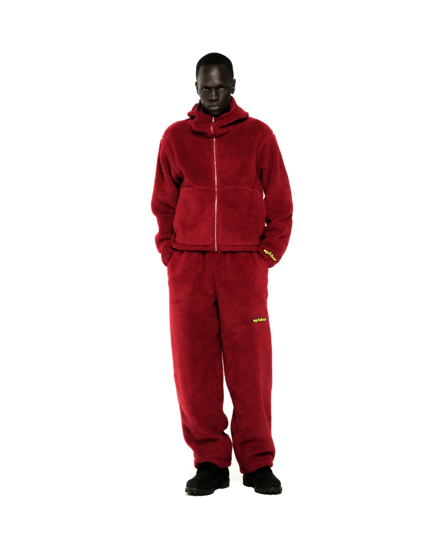 Dark-skinned model wearing a red sherpa fleece zip-up hoodie and matching sweatpants with yellow logos.