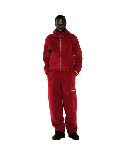 Dark-skinned model wearing a red sherpa fleece zip-up hoodie and matching sweatpants with yellow logos.