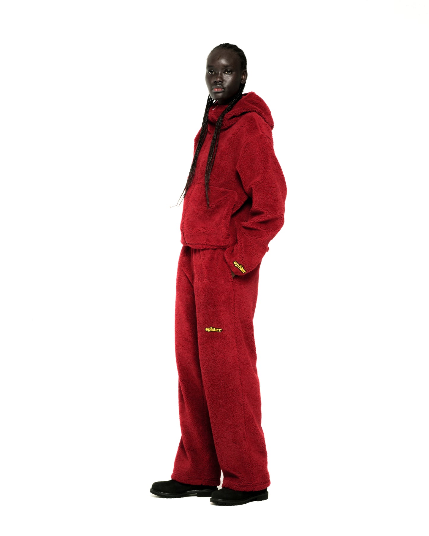 Dark-skinned model in a red sherpa fleece zip-up hoodie and matching sweatpants with yellow logo embroidery.