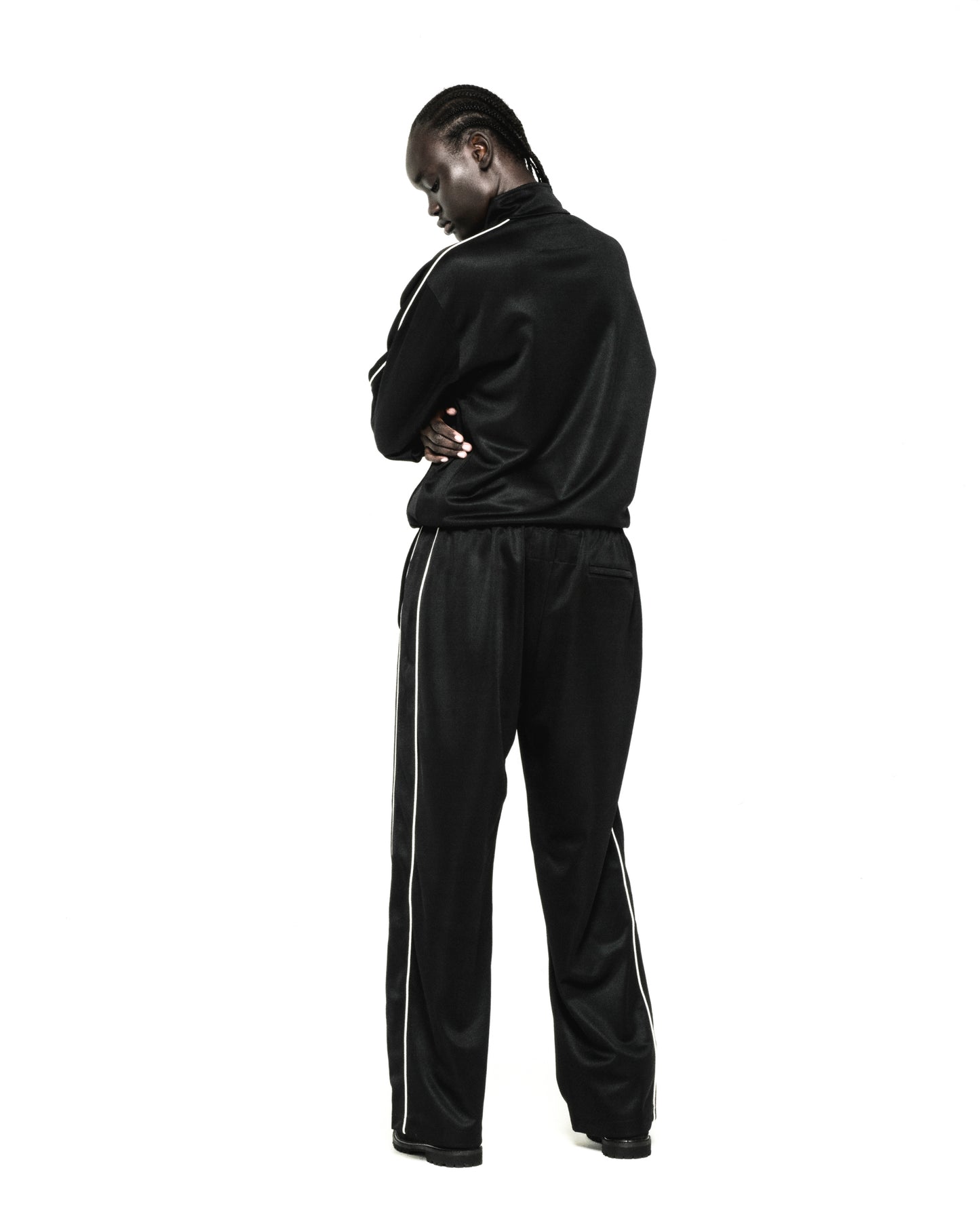 Black polyester track jacket and pants with white piping, worn by a person facing away.