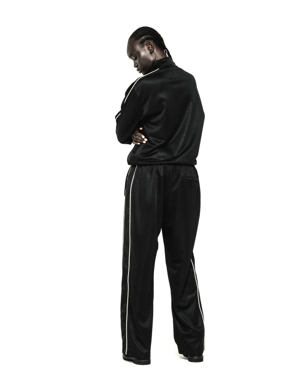 Black polyester track jacket and pants with white piping, worn by a person facing away.