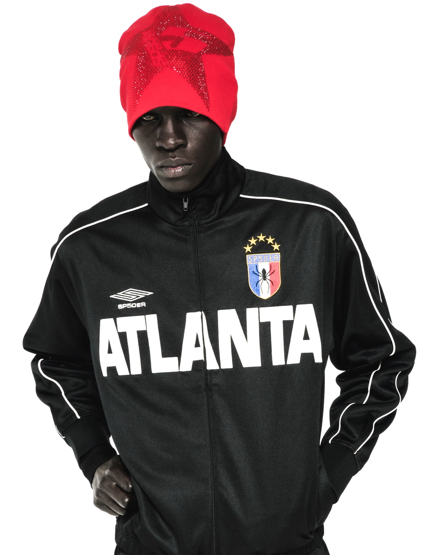 Red acrylic skully with rhinestone 5-star design worn by a model in a black track jacket.