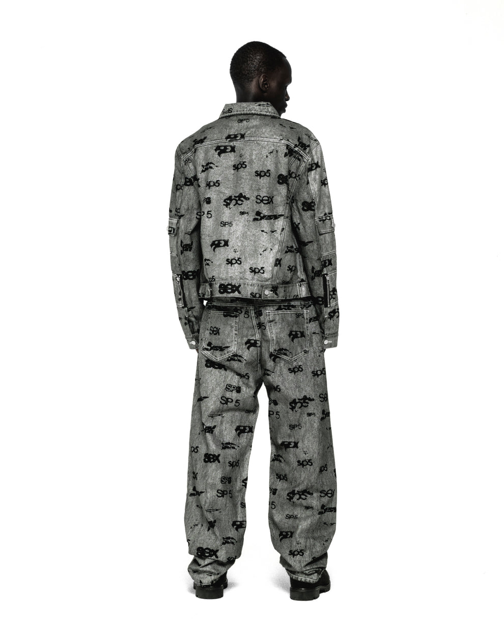 Model from behind wearing a grey denim trucker jacket and matching jeans with an all-over "SEX" print.