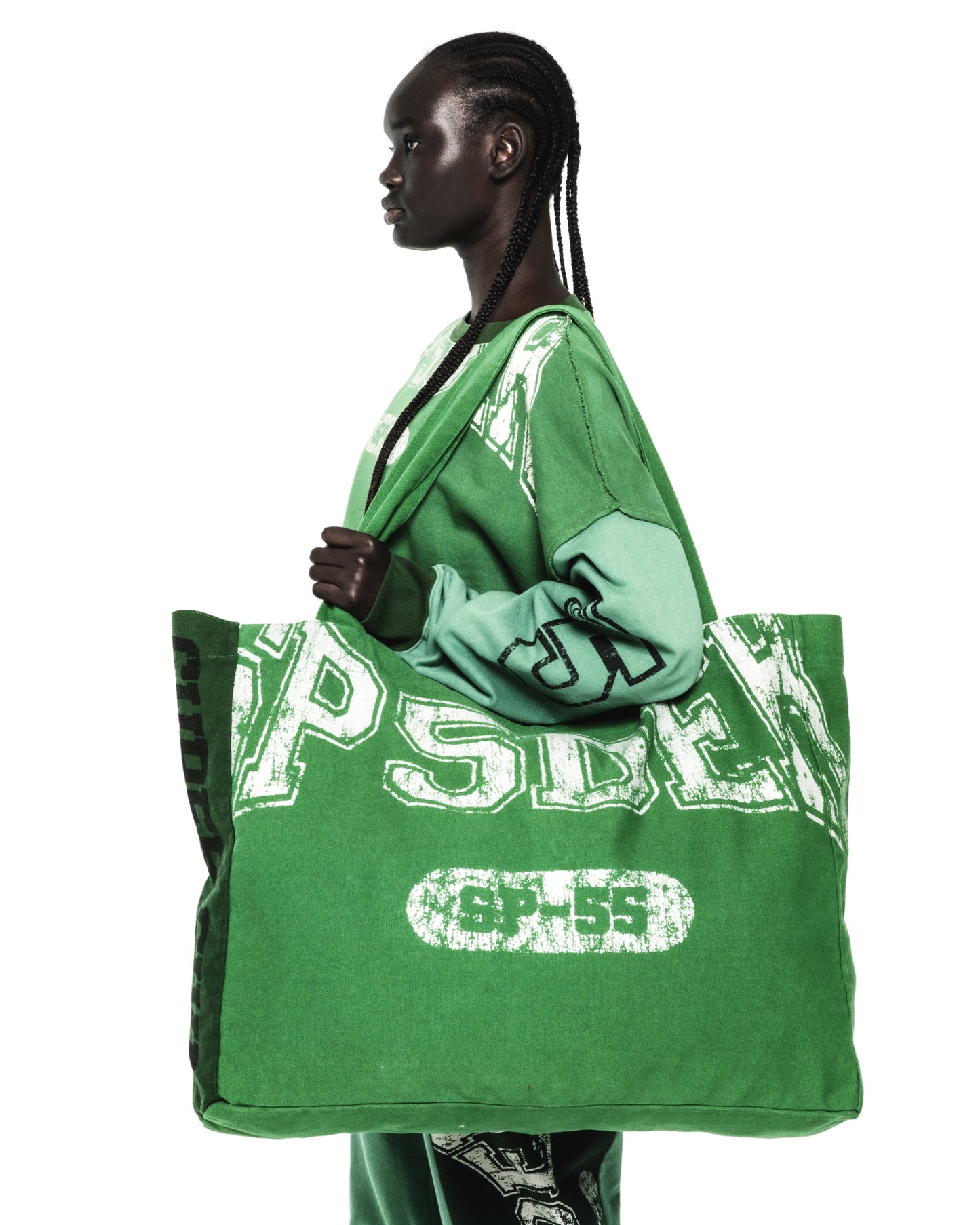 Model carries a large green SUPERFIVE TOTE made of 8oz brushed twill with white SP5DER graphic print.