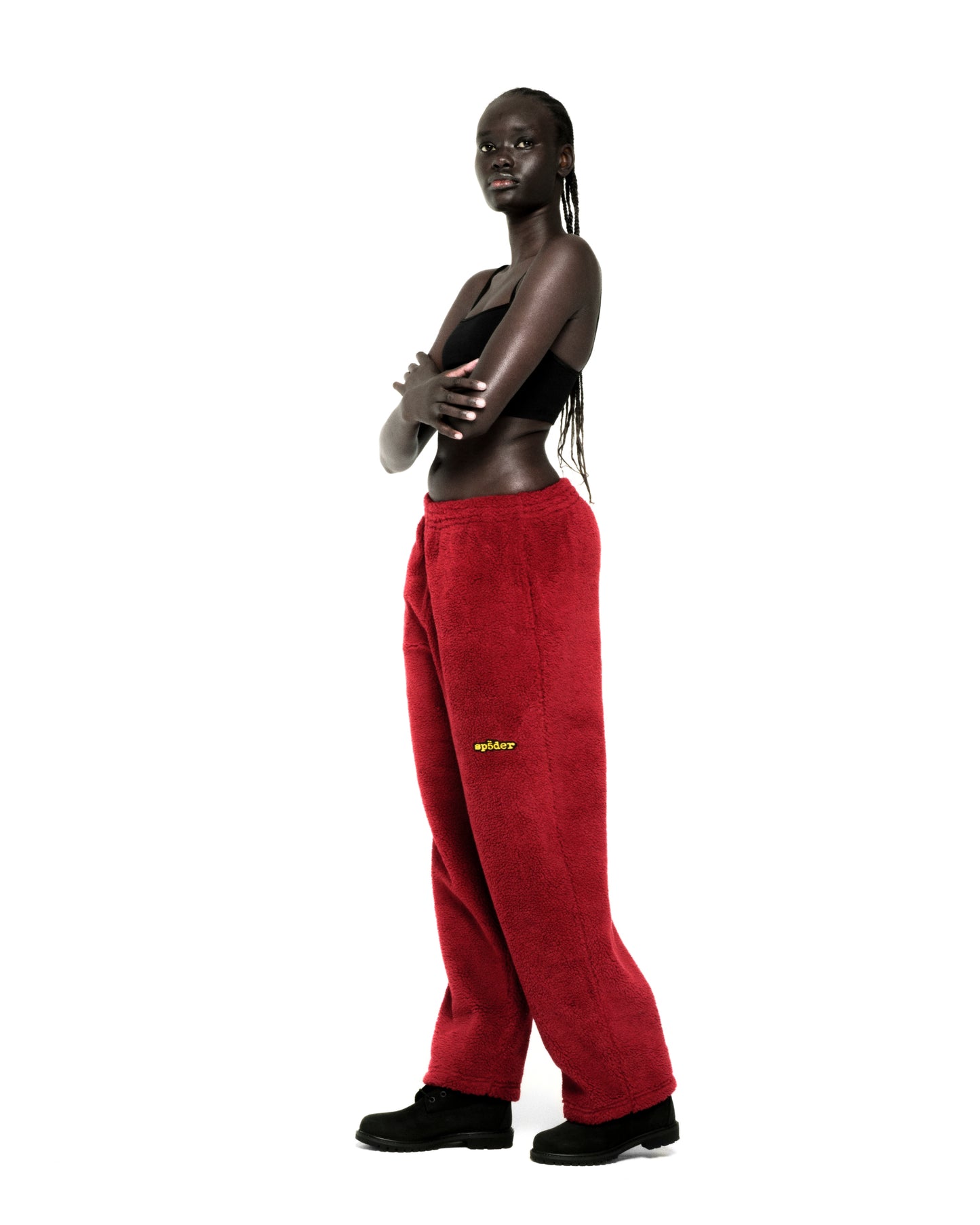 Model wearing red sherpa fleece pants with yellow rubberized logo patch and black sports bra.