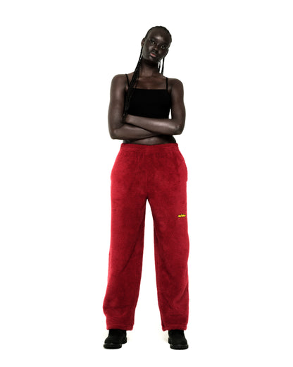 Model wearing red teddy fleece pants with a yellow rubberized logo patch and a black tank top.