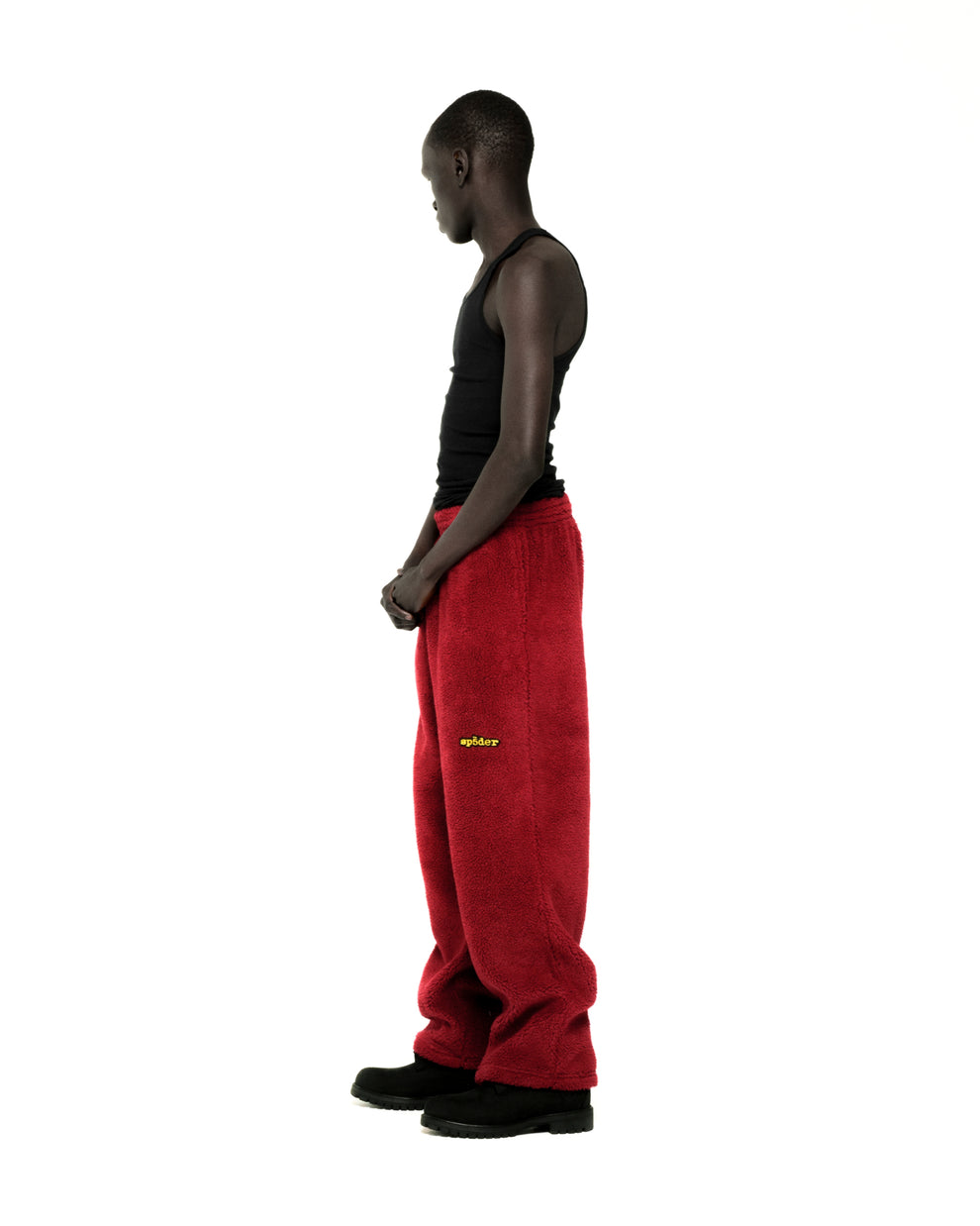 Man in red teddy fleece pants with yellow rubberized logo patch, black tank top, and black boots.