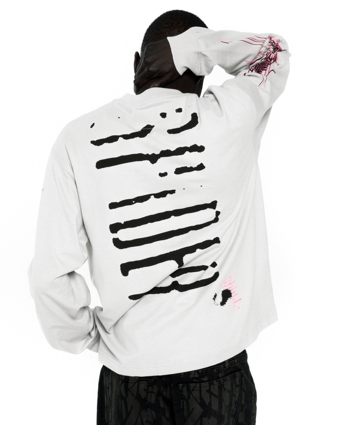 White 100% cotton long sleeve tee with black graphic print on back and pink graphic on sleeve.