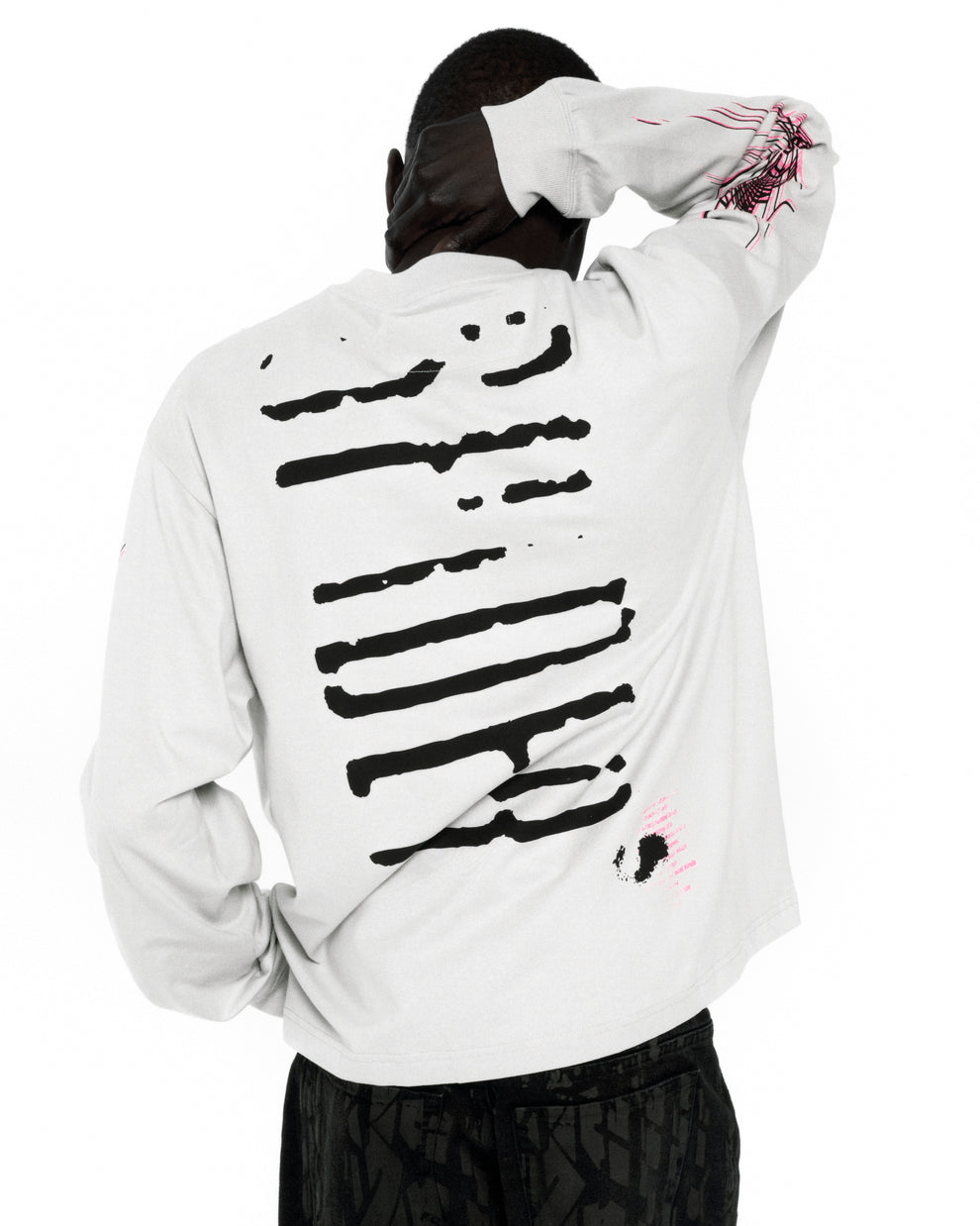 White 100% cotton long sleeve tee with black graphic print on back and pink graphic on sleeve.