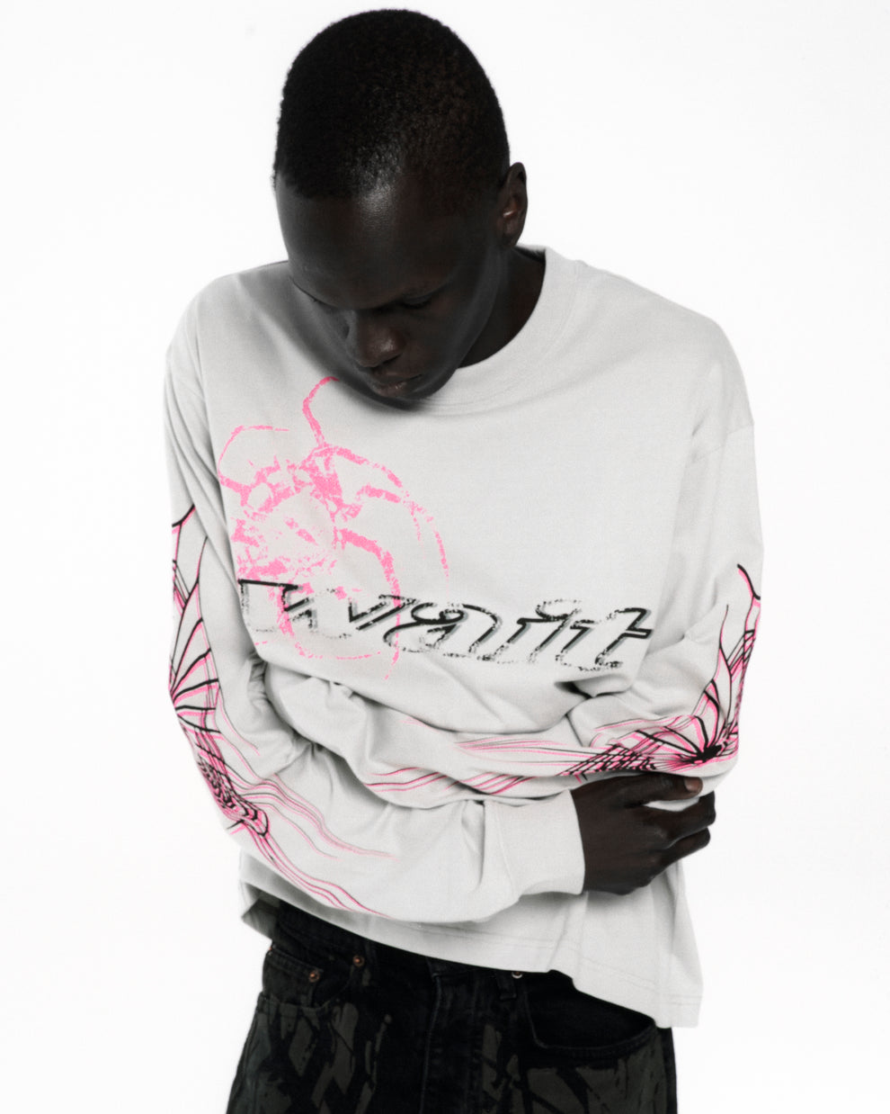 White 100% cotton long sleeve tee with pink and black graphic print on front and sleeves.