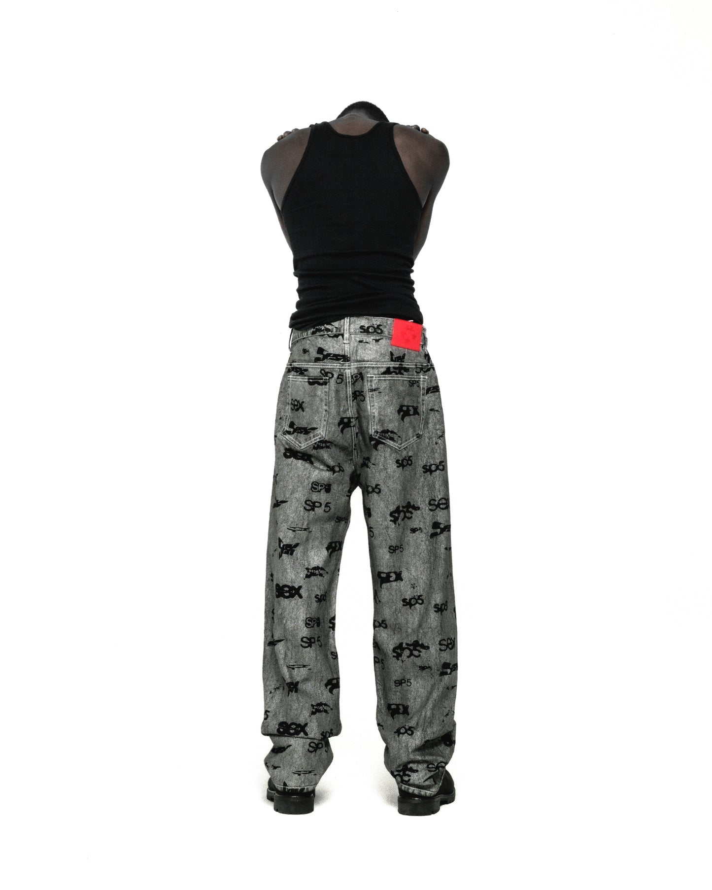 Gray denim pants with all-over black "SEX" and "SP5DER" print, red leather patch, and straight leg fit.
