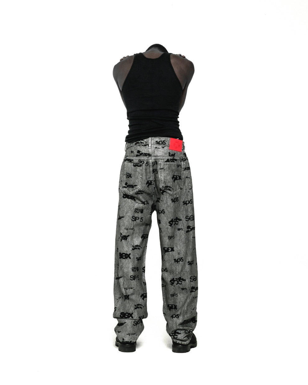 Gray denim pants with all-over black "SEX" and "SP5DER" print, red leather patch, and straight leg fit.