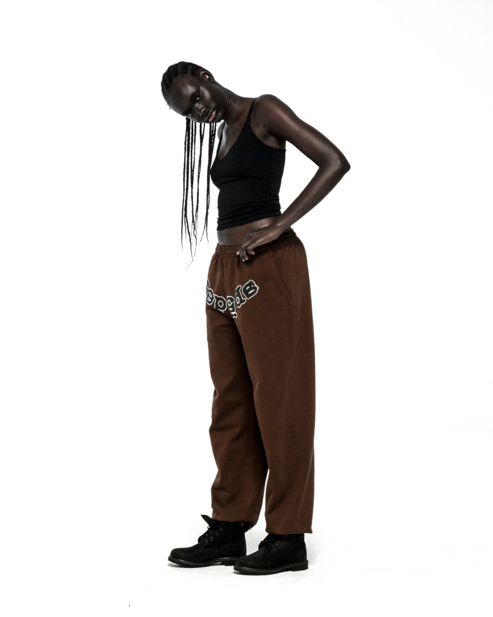 Brown fleece sweatpants with "SP5DER" rhinestone logo on crotch, worn by a model.