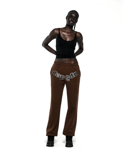 Dark-skinned model wearing brown RHINESTONE OG LOGO SWEATPANTS with "SP5DER" text across the crotch.