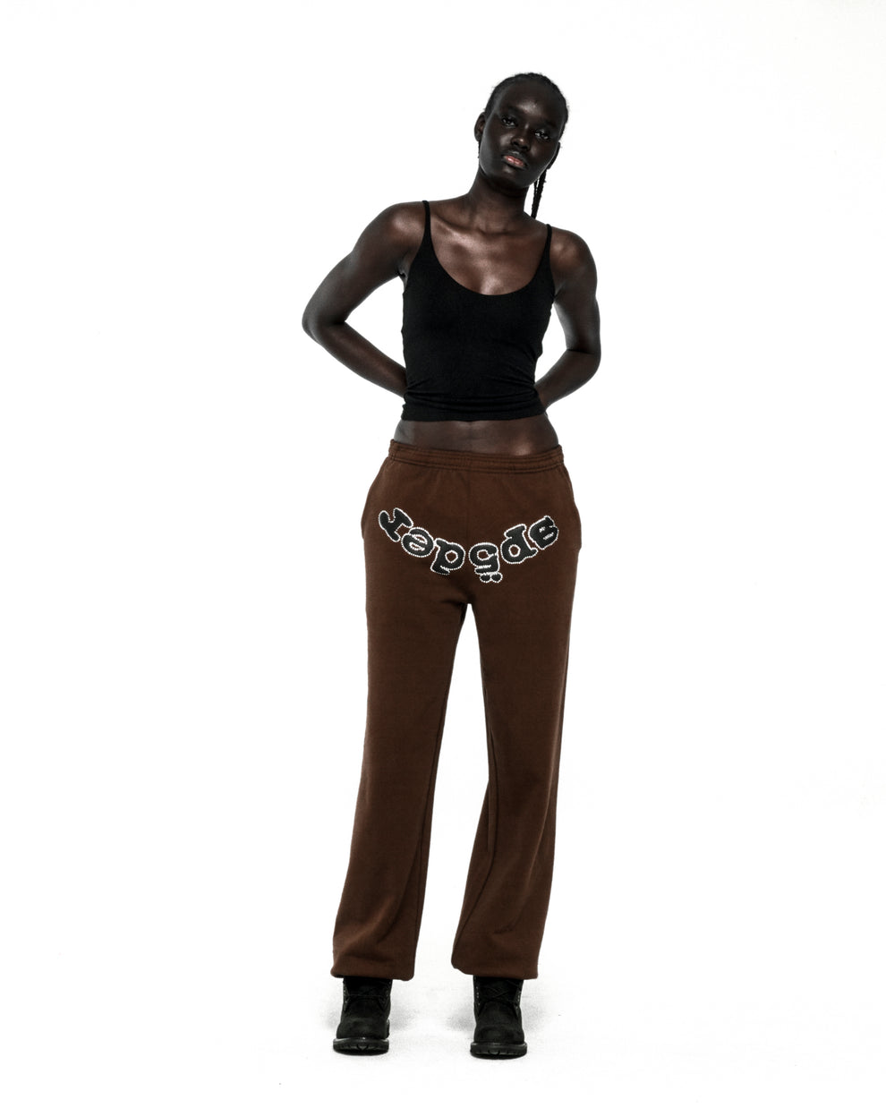 Dark-skinned model wearing brown RHINESTONE OG LOGO SWEATPANTS with "SP5DER" text across the crotch.