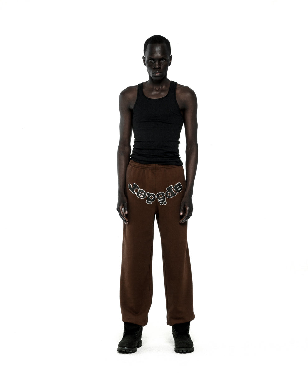 Brown fleece sweatpants with "SP5DER" rhinestone text on the crotch, worn by a model.