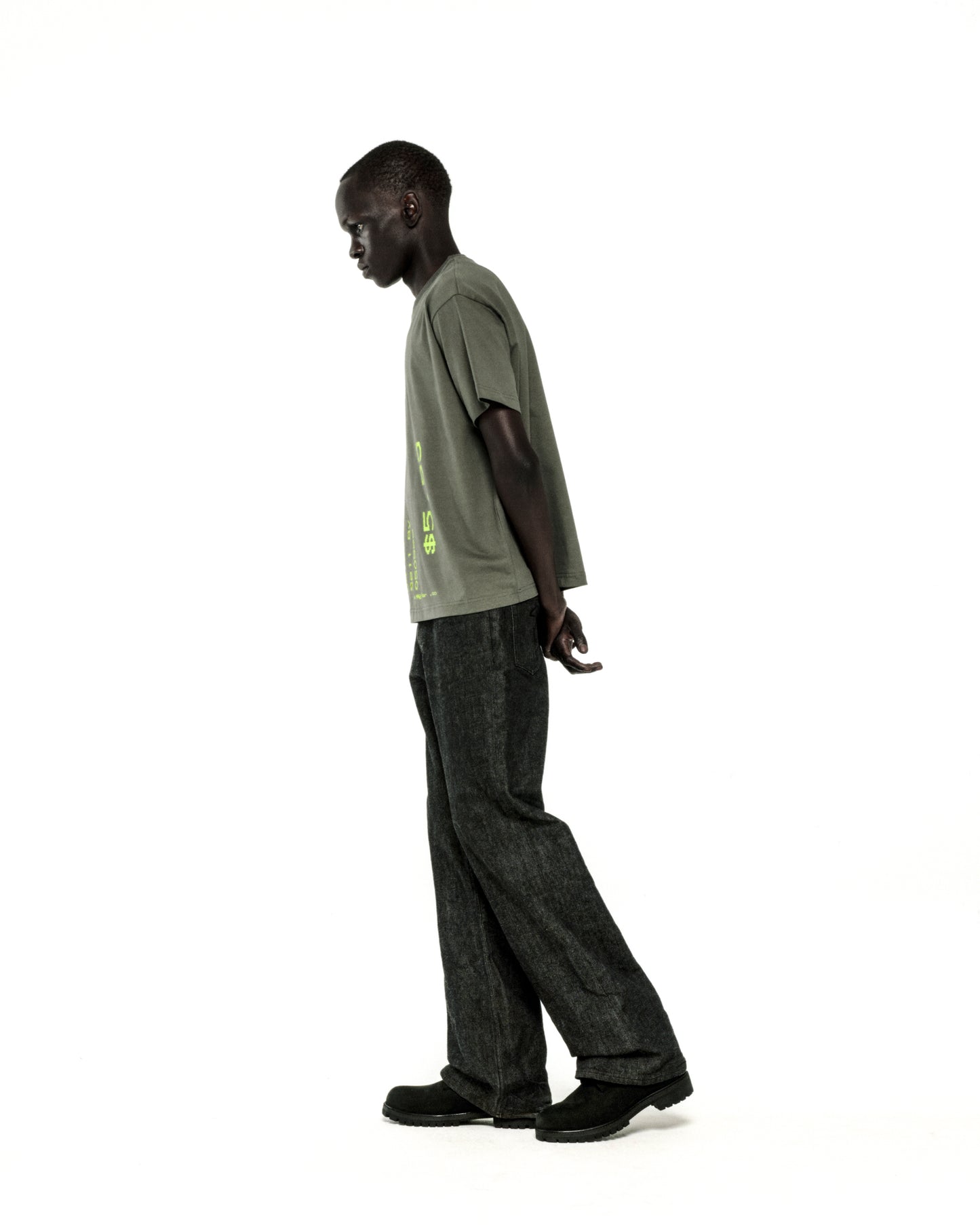 Man in standard fit olive green cotton tee with graphic print, dark jeans, and black shoes.