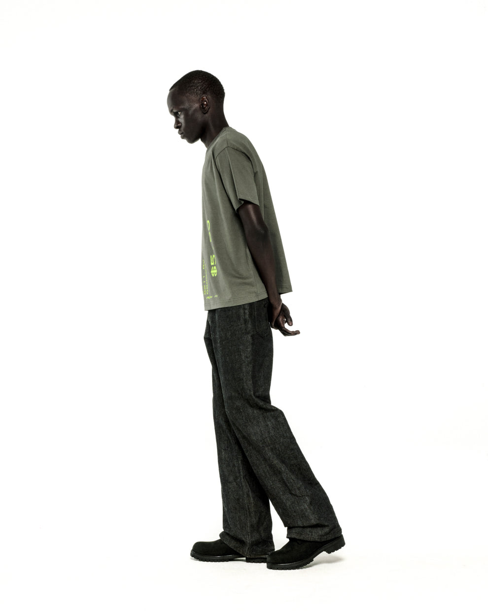 Man in standard fit olive green cotton tee with graphic print, dark jeans, and black shoes.
