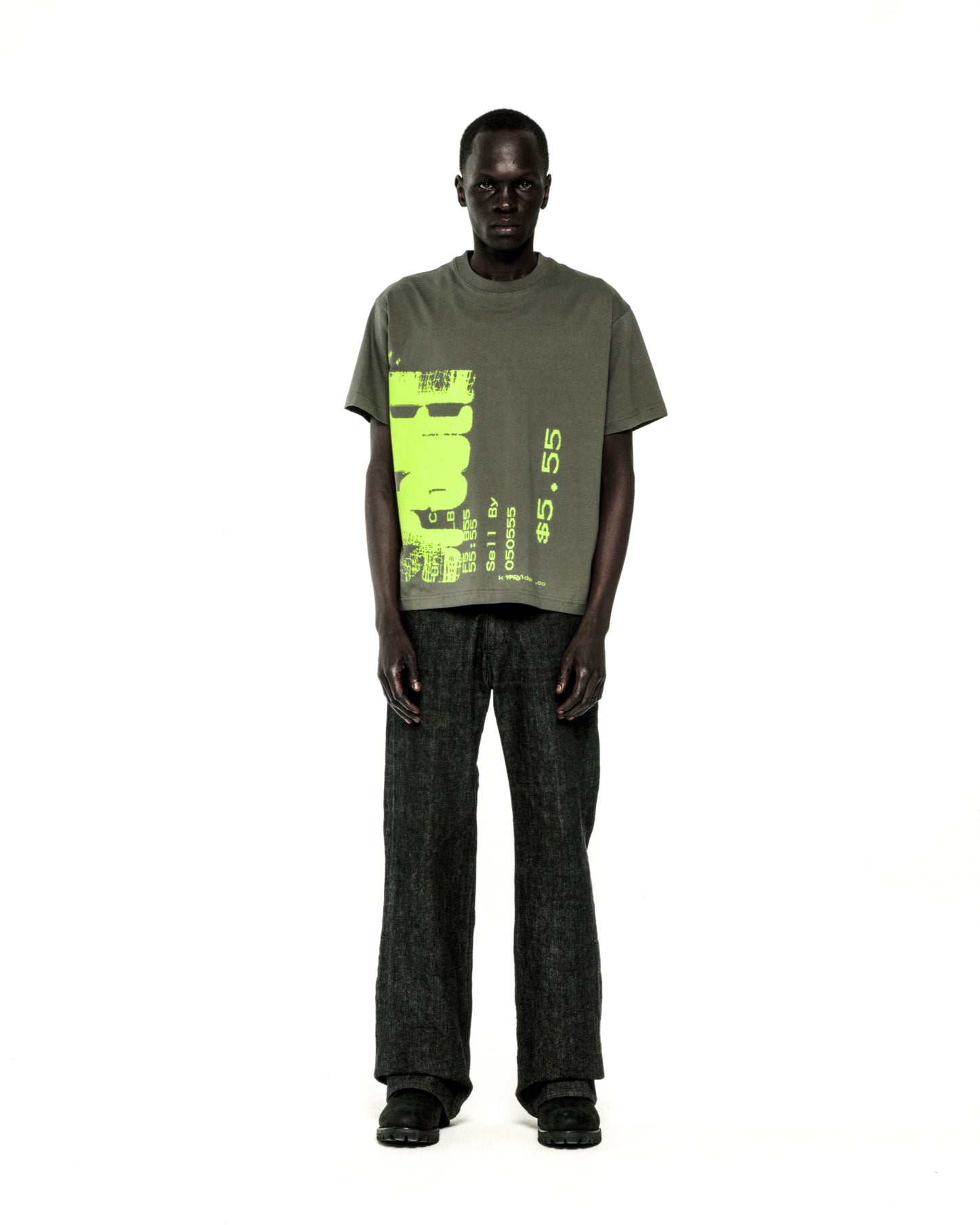Man in standard fit olive green cotton COMMERCE TEE with neon yellow graphic print and dark pants.