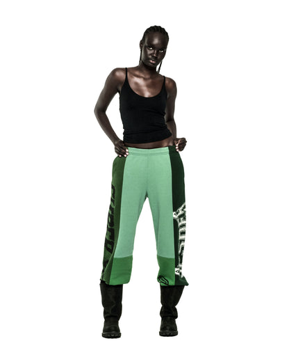 SUPERFIVE SWEATPANT: Model in wide-leg, contrast-paneled green cotton fleece sweatpants with graphic print and raw hem.