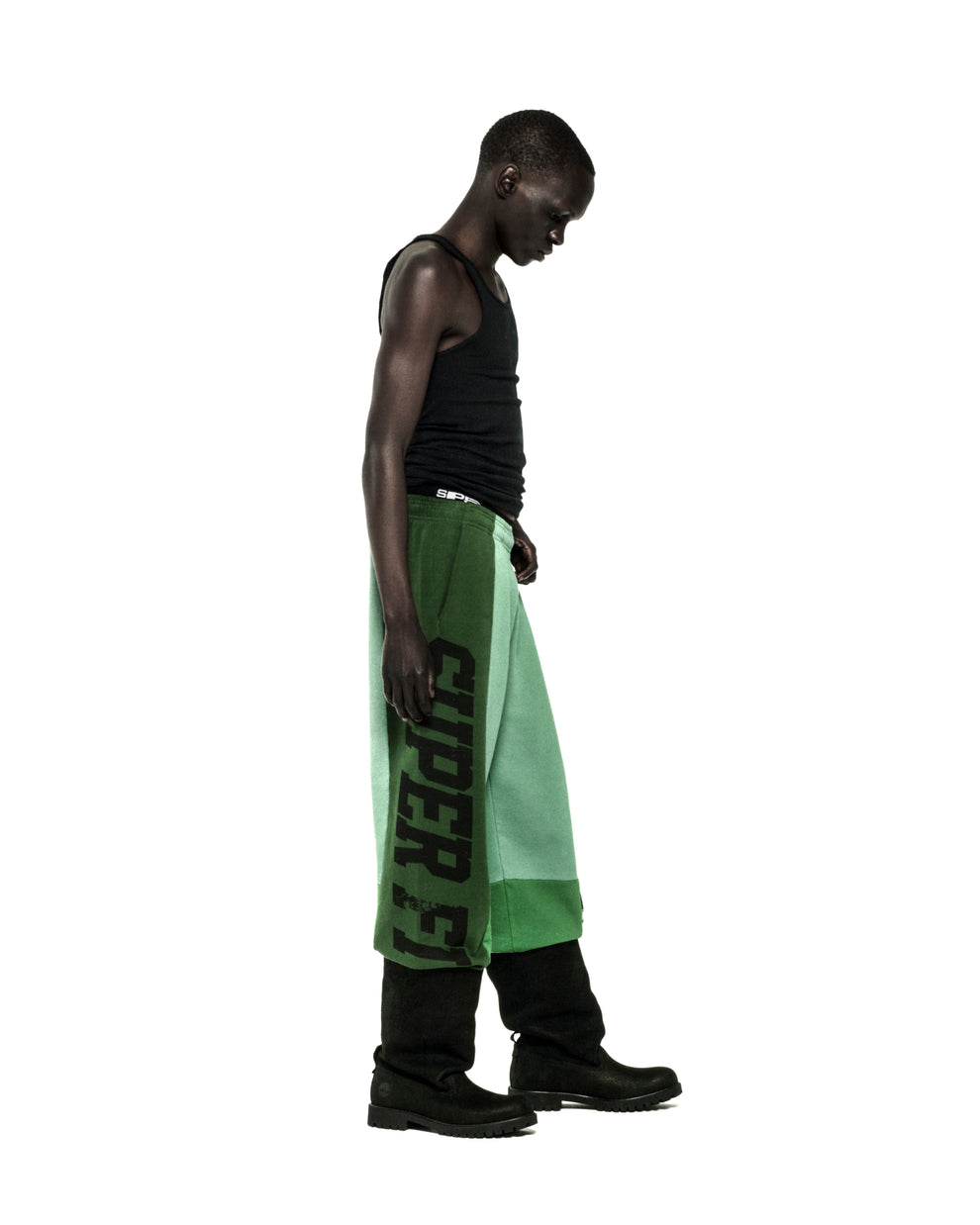 SUPERFIVE SWEATPANT: Black model in wide-leg, contrast panelled green cotton fleece sweatpants with "SUPERFIVE" graphic.