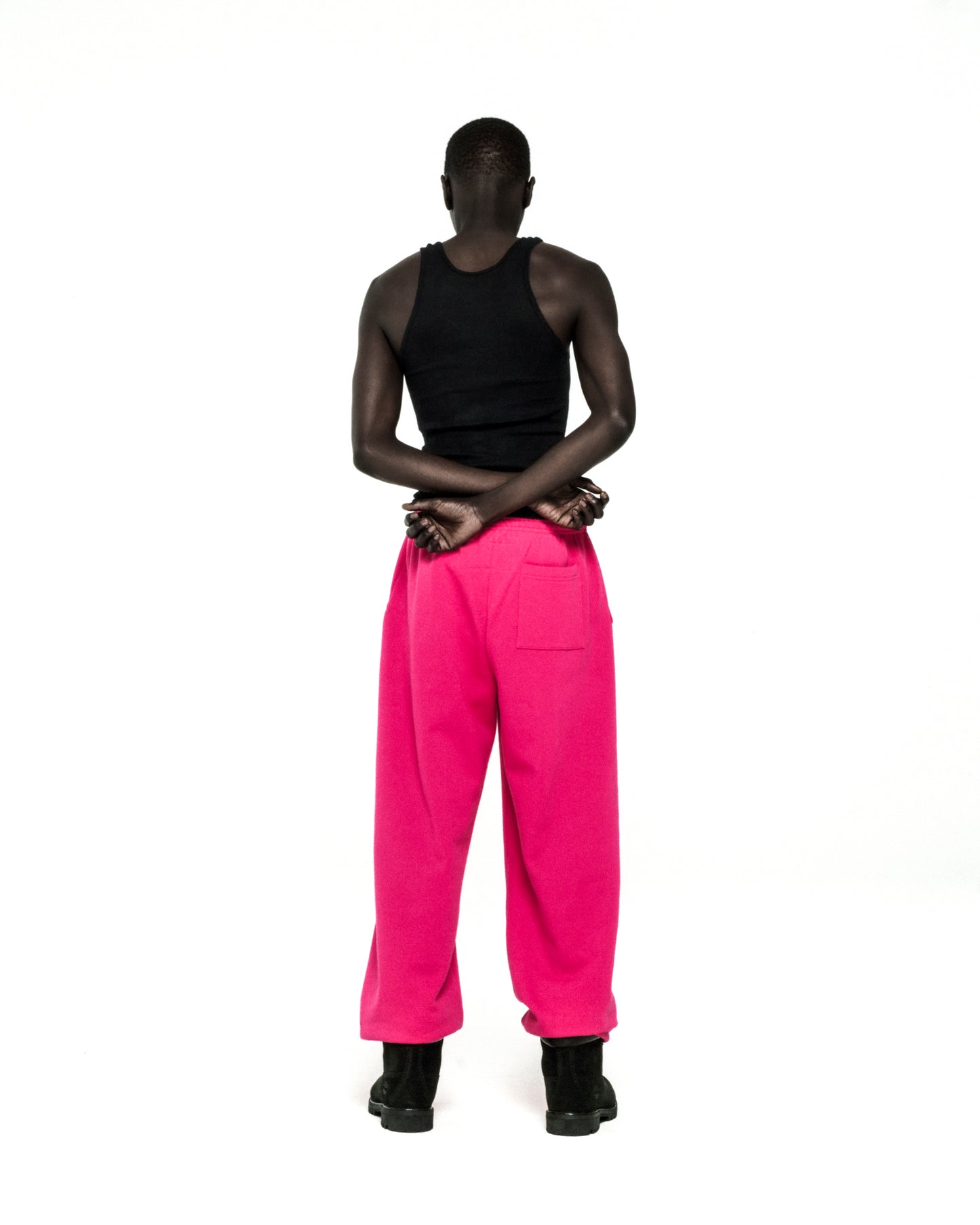 Model from behind wearing bright pink ANGEL NUMBER SWEATPANTS with elasticized cuffs and a black tank top.