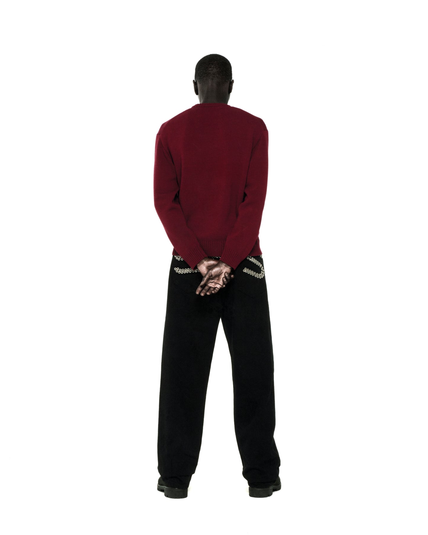 Back view of a person wearing a dark red knit sweater with ribbed collar, hem, and cuffs, paired with black pants.