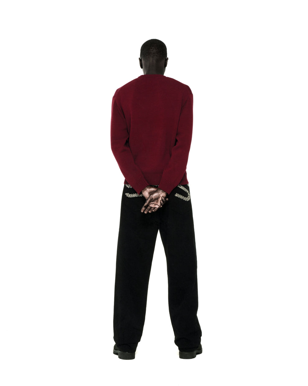 Back view of a person wearing a dark red knit sweater with ribbed collar, hem, and cuffs, paired with black pants.