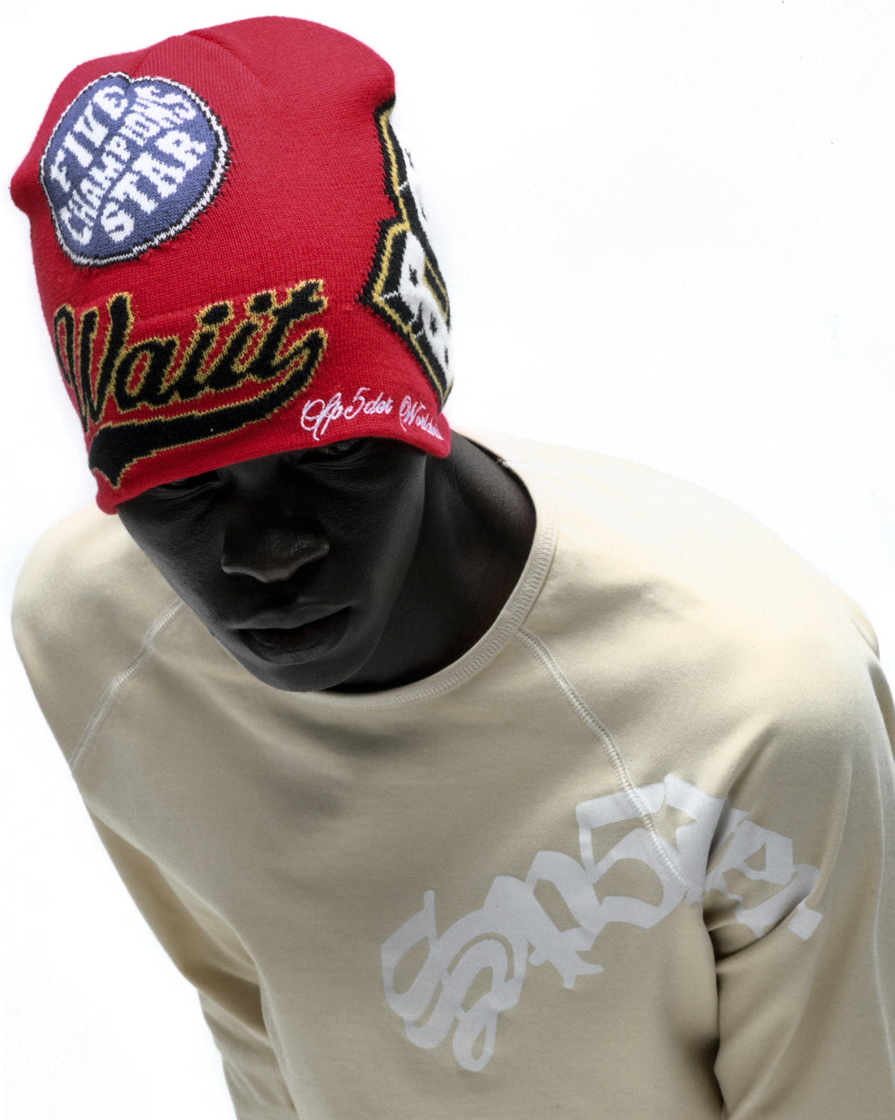 Red acrylic DISTRICT V SKULLY beanie with varsity graphic patches and "Wait" embroidery on a model.