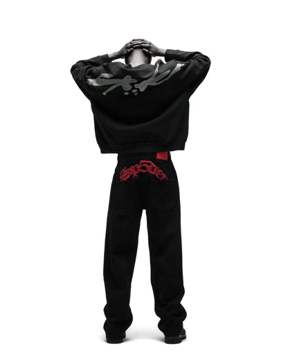 Black cotton crewneck with rhinestone graphic on back, paired with black jeans featuring red embroidered text.
