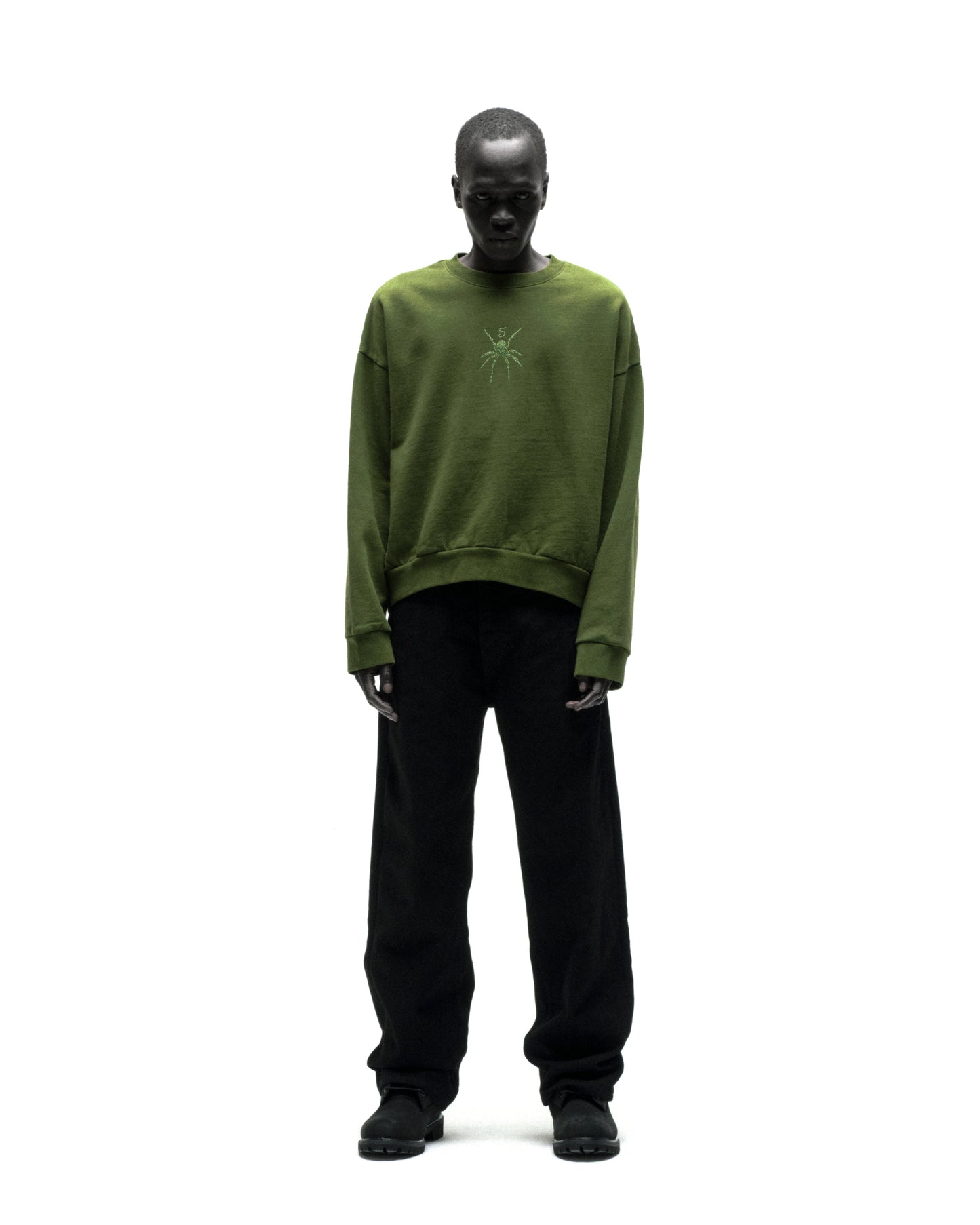 Model wearing a green RHINESTONE TM CREWNECK, 100% cotton brushed fleece with spider graphic.