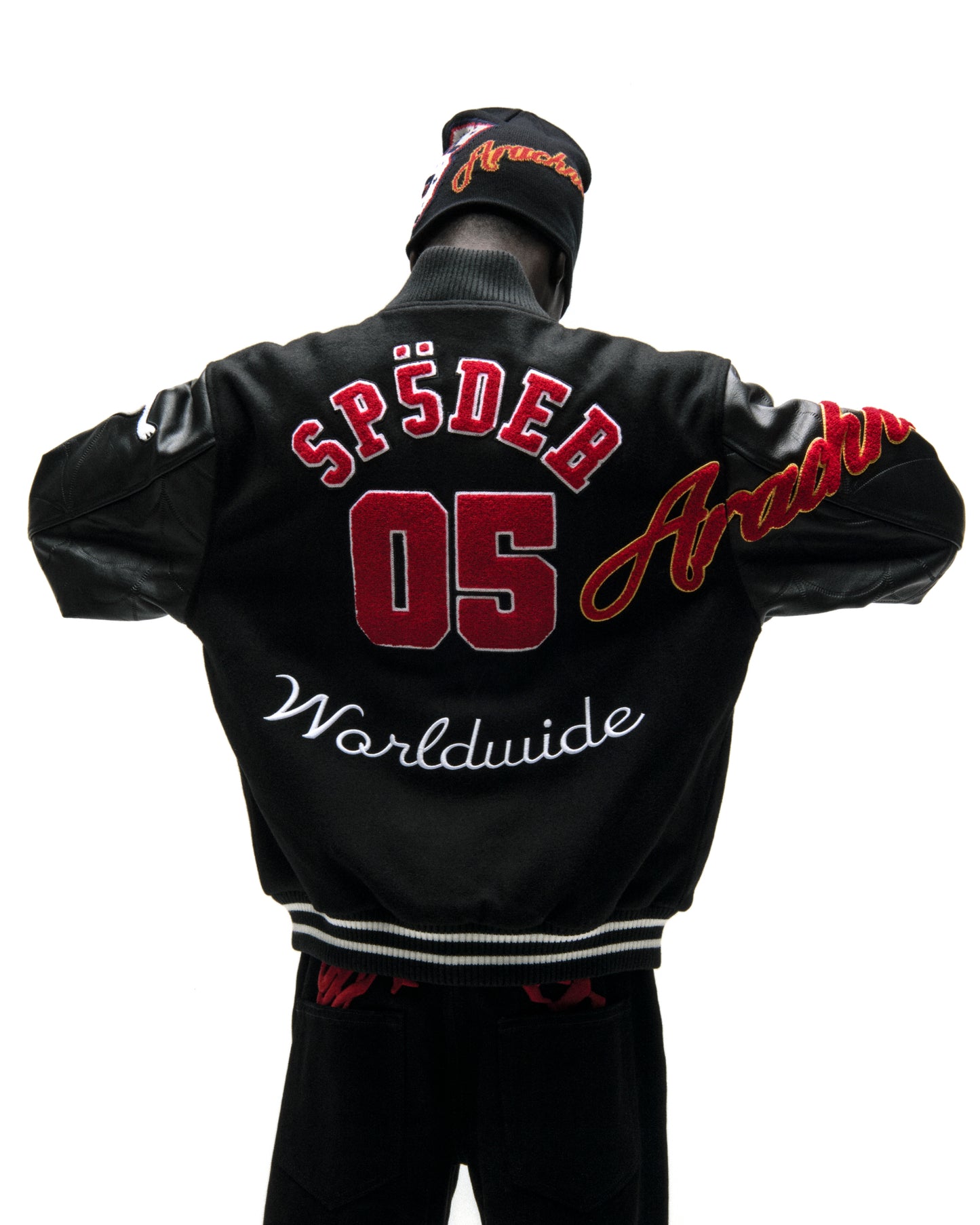 Black wool varsity jacket with leather sleeves, red "SP5DER 05" and "Worldwide" embroidery, and a matching beanie.