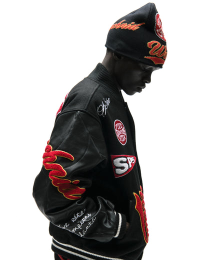Black wool varsity jacket with leather sleeves, debossed web design, and red embroidered patches.