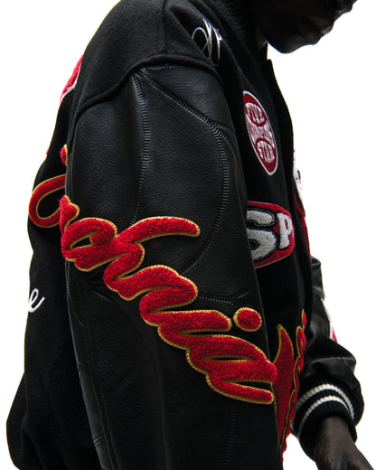 Black wool varsity jacket with contrasting leather sleeves, debossed web design, and red embroidered patches.