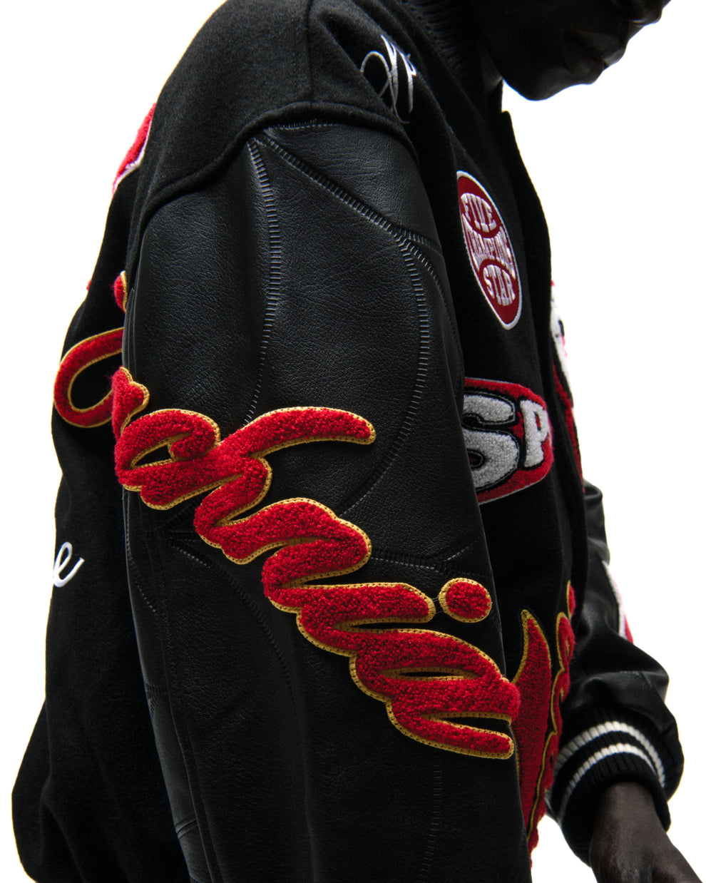 Black wool varsity jacket with contrasting leather sleeves, debossed web design, and red embroidered patches.