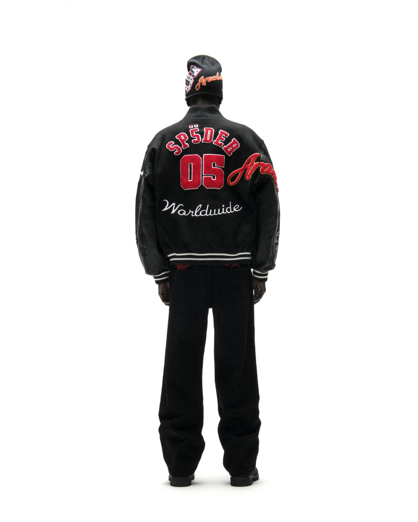 Black wool varsity jacket with leather sleeves, red "SP5DER 05" embroidery, and "Worldwide" script on the back.